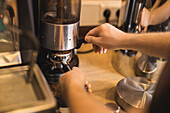 High angle of crop anonymous barista preparing fresh ground coffee in portafilter of professional grinder in cafe