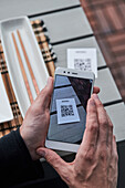 Ernte von oben, nicht erkennbarer Mann, der ein Smartphone benutzt und den QR-Code der Speisekarte eines Restaurants scannt