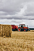Getrocknete Heurolle und moderner Traktor auf landwirtschaftlichem Feld in bergigem Gebiet im Sommer