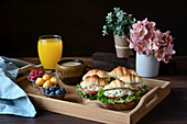 Delicious croissant sandwiches with vegetables served on tray with cappuccino and orange juice prepared for French breakfast and placed on wooden table