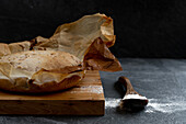 Composition with freshly baked rustic sourdough round bread loaf on parchment paper placed on wooden board with spoon and wheat flour