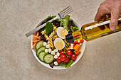 Cook adding olive oil from bottle into bowl with healthy food and stainless steel fork on stone table