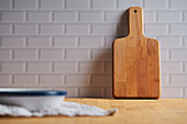 Wooden chopping board placed near wall on table with bowl in light kitchen