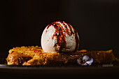 Niedriger Blickwinkel auf leckeren French Toast mit Baiser-Milch-Eiskugel, bedeckt mit süßer Beerensauce auf einem Teller mit Gewürzen in einem Restaurant auf dunklem Hintergrund