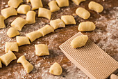 Draufsicht auf weiche, rohe Teigstücke, die während der Zubereitung von Gnocchi in der Küche auf einem mit Mehl bestäubten Holztisch neben einem Schneidebrett liegen