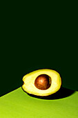 Eine halbe reife Avocado mit Samen liegt in einer Tischecke vor einem dunkelgrünen Hintergrund