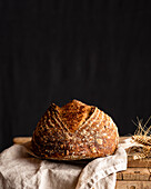 Delicious whole artisan bread with crust on crumpled fabric against wheat spikes on wooden surface