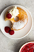 Top view of tasty bitten doughnut sprinkled with powdered sugar served on plate with fresh raspberries on gray background with jam