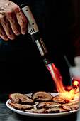 Stock photo of unrecognized chef using kitchen torch in restaurant.