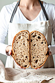 Crop faceless woman hands holding freshly baked sourdough rye bread Crumb white cutting in half