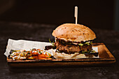 Leckerer Burger mit vegetarischem Patty und gegrillten Shiitakes zwischen Brötchen neben Süßkartoffel- und Karottenscheiben mit Alioli-Sauce auf dunklem Hintergrund