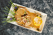 From above delicious ossobuco dish with vegetable and rice sauce garnished with flowers on rectangular plate on marble table during lunch in restaurant