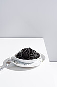 Minimalistisches Studio mit schwarzen Tintenfischspaghetti in einer vollen Keramikschale auf einem weißen Tisch