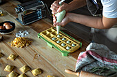 Unrecognizable person preparing raviolis and pasta at home. She is filling the ravioli with a pastry bag.