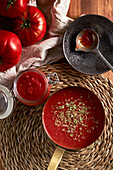 Top view of pan and container with delicious homemade tomato sauce sprinkled with oregano placed on woven mat on wooden table in kitchen