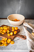 Pile of fresh orange cut kumquats on wooden chopping board placed on marble table with towel in kitchen