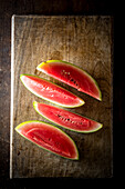 Hoher Winkel von Scheiben reifer süßer Wassermelone auf Holztisch vor dunklem Hintergrund