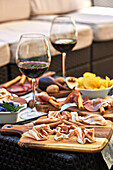 Delicious bacon served on wooden cutting board on table with various appetizers and glasses of red wine