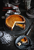 From above of piece of sweet tasty appetizing cheesecake served on plate with spoon on gray table near pie placed on baking pan with knife