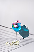 Transparent glass of fresh cocktail with mint leaves and flowers placed on surface against white background