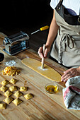 Unrecognizable person preparing raviolis and pasta at home. She is painting the pasta with eggs