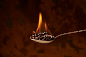 Nahaufnahme eines Löffels voll mit einem Haufen gerösteter Kaffeebohnen mit Feuer auf braunem Hintergrund