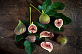 Top view of whole and cut figs with juicy pulp on green foliage with veins on wooden surface