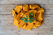 Top view of pile of pieces of ripe pumpkin garnished with fresh sprig of parsley placed on wooden table