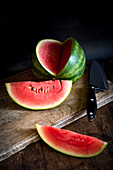 Hoher Winkel von Scheiben der reifen süßen Wassermelone auf Holztisch mit Messer auf dunklem Hintergrund