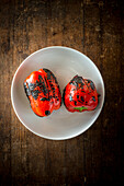 Top view of delicious whole grilled red peppers in round shaped ceramic bowl on brown background