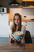 Young female looking at camera with round shaped bowl full of delicious corn rings in milk for breakfast at home