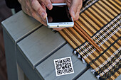 Ernte von oben, nicht erkennbarer Mann, der ein Smartphone benutzt und den QR-Code der Speisekarte eines Restaurants scannt