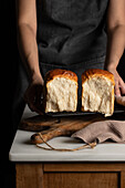 Unrecognizable crop baker taking split halves of sandwich bread from grill tray located on counter in dim light