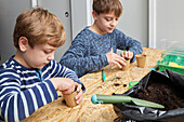 Geschwister pflanzen Setzlinge in einem Pappbecher mit Erde auf einem Tisch mit einer Gartenschaufel