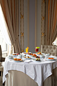 Verschiedene bunte Gerichte und Säfte, die beim Frühstück in einem eleganten Hotelrestaurant an einem sonnigen Morgen auf einem runden Tisch serviert werden