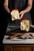 Unbekannter Erntebäcker, der geteilte Hälften von Sandwichbrot von der Grillplatte auf dem Tresen im gedämpften Licht nimmt