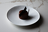 Blick von oben auf einen leckeren Schokoladenkuchen mit essbarer Dekoration auf einem weißen Teller und auf einem Marmortisch