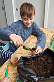 Happy kid with gardening shovel filling eco cup with earth at table