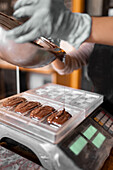 Cropped unrecognizable person in apron and gloves filling plastic mold on digital scale with liquid chocolate during work in confectionery in daytime