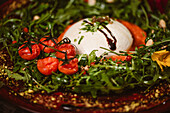 Leckerer Burrata-Käse auf kalter Tomatencreme mit Rucolablättern und Kirschtomaten mit Trüffeln und Erdnüssen