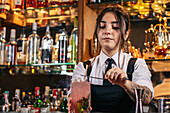Young woman in uniform putting straw on top of strawberry mojito while working in bar at night