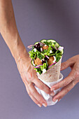 Cropped unrecognizable person hands holding vegan falafel wrap on colorful purple background