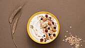 From above yoghurt served with oats and dried nuts on brown background