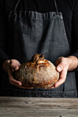 Unrecognizable crop chef in apron standing with piece of freshly baked bread