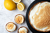 Top view of appetizing meringue pie served on marble table with fresh lemons in kitchen