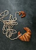 From above of delicious freshly baked traditional croissant wrapped with rope on black background
