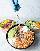 Crop unrecognizable chef decorating bowl with tasty poke dish served on marble table