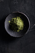 Draufsicht auf pulverisierte Grünteeblätter in einer Steinschale auf einem schwarzen Tisch für Tee und Gewürze