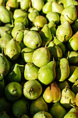 From above full frame background of fresh ripe green pears stacked together on stall in local market with bright sunlight