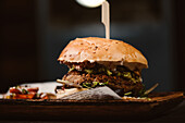 Niedriger Winkel eines leckeren Burgers mit vegetarischem Patty und gegrillten Shiitakes zwischen Brötchen neben Süßkartoffel- und Karottenscheiben mit Alioli-Sauce auf dunklem Hintergrund